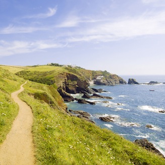 Coast Path on the clifftop, heading towards Lizard Lighthouse under a blue sky with wispy clouds