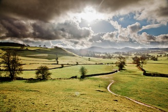 Open countryside cross-crossed by stone walls. Wintery sun shining through grey clouds